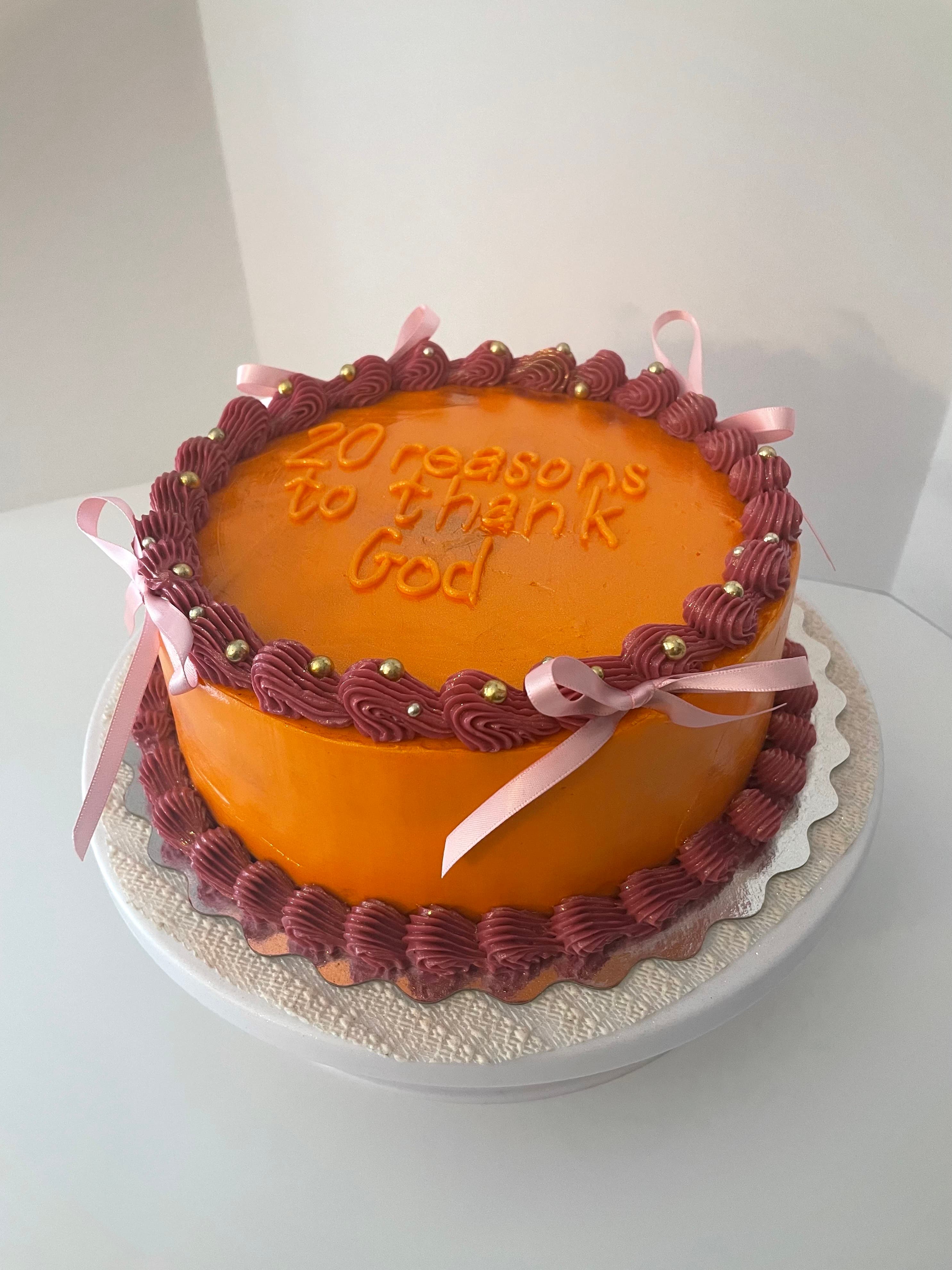 Sunset birthday cake with orange frosting, mauve piping, gold pearls, and pink ribbons